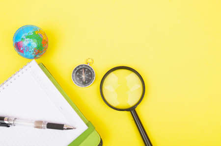 conceptual image. Notebook, compass, magnifying glass, pen and world globe on yellow background.の写真素材