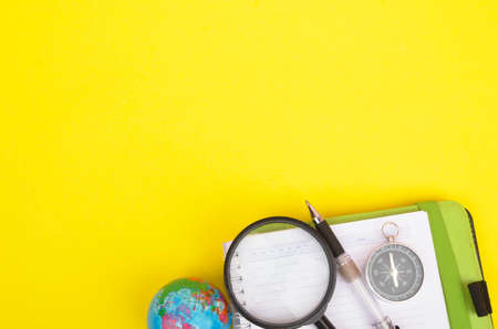 conceptual image. Notebook, compass, magnifying glass, pen and world globe on yellow background.の写真素材