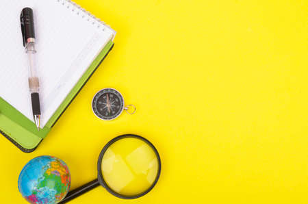 conceptual image. Notebook, compass, magnifying glass, pen and world globe on yellow background.の写真素材