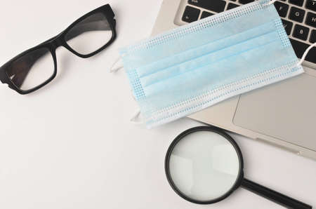 White office desk table face mask, magnifying glass. eye glass with laptop on white background. Work from home and covid-19 concept new normal. Selective focus.の写真素材