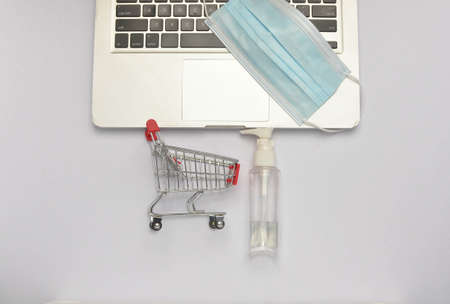 Shopping trolley and medical face mask with laptop on white background. Covid-19 pandemic. Online shopping. Selective focus.の写真素材