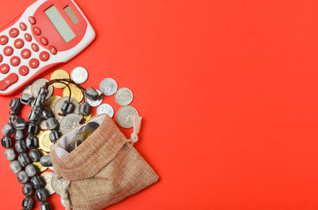 Rosary with coins in a gunny sack and calculator on red background. Islamic banking or financing concept. Top view and selective focus.の写真素材