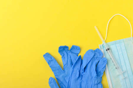 Medical glove with syringe and medical face mask on yellow background. Top view and selective focus.