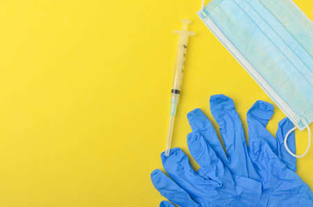 Medical glove with syringe and medical face mask on yellow background. Top view and selective focus.の写真素材