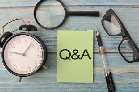 Top view of a magnifying, pen, alarm clock and spectacles with text Q&A on wooden background.Selective focus.の写真素材