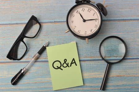 Top view of a magnifying, pen, alarm clock and spectacles with text Q&A on wooden background.Selective focus.の写真素材