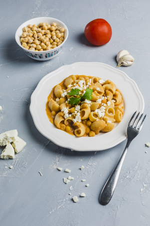 pasta Pipa the rigat with a sauce of chickpeas and tomatoes, sprinkled with feta cheese and cilantro on a white plate on a light grey background high angleの写真素材