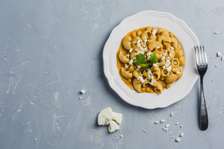 pasta Pipa the rigat with a sauce of chickpeas and tomatoes, sprinkled with feta cheese and cilantro on a white plate on a light grey background high angleの写真素材