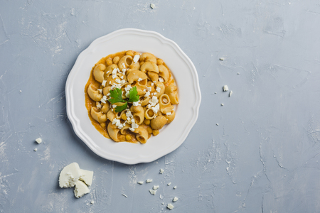 pasta Pipa the rigat with a sauce of chickpeas and tomatoes, sprinkled with feta cheese and cilantro on a white plate on a light grey background high angleの写真素材