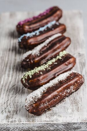 chocolate eclairs with colored powder on a white wooden Board and a light background top view with copyspace focus on one dessertの写真素材