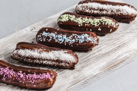 chocolate eclairs with colored powder on a white wooden Board and a light background top view with copyspace focus on one dessertの写真素材