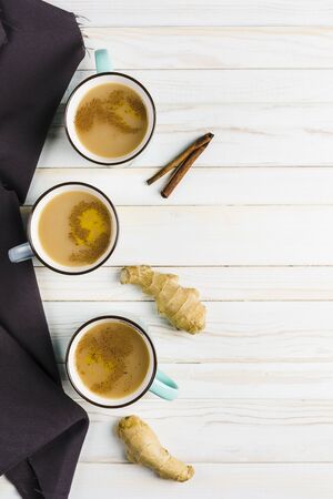 Masala tea in ceramic cups with the winter spices of cinnamon and ginger on a light wooden background top view with copyspaceの写真素材