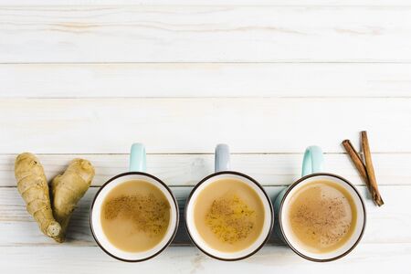 Masala tea in ceramic cups with the winter spices of cinnamon and ginger on a light wooden background top view with copyspaceの写真素材