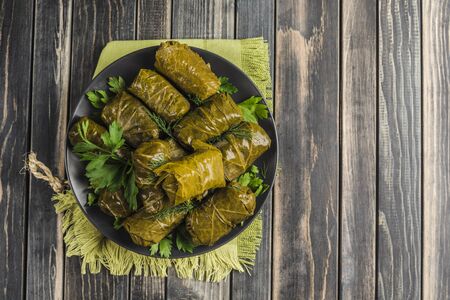 Delicious stuffed grape leaves (traditional doom Mediterranean cuisine Dolma) on a black plate with fresh cilantro and dill on dark wooden background top view with copyspaceの写真素材
