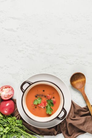 Spanish cold gazpacho soup with tomatoes, pepper, garlic and fresh herbs in a dark plate on a light background top view with copyspace. Vegetarian food for health. Flat lay.の写真素材