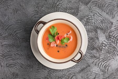 Spanish cold gazpacho soup with tomatoes, pepper, garlic and fresh herbs in a dark plate on black background top view with copyspace. Vegetarian food for health. Flat lay.の写真素材