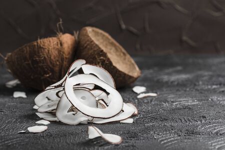Coconut chips on a black background, in the background two coconuts, side view close-up, a natural product for healthy nutrition.の写真素材