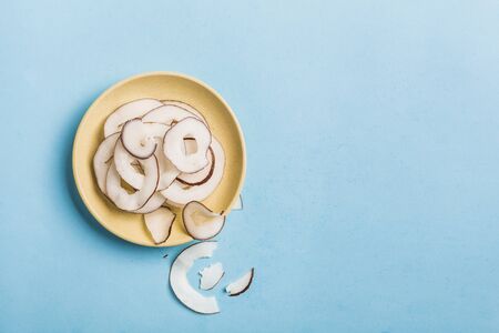Coconut chips in a yellow plate on a blue background, flatlay, a natural product for healthy nutrition. Concept.の写真素材