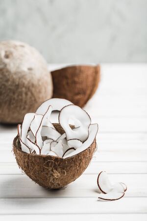 Coconut chips in a brown bowl on a white wooden background, side view close-up, a natural product for healthy nutrition.の写真素材