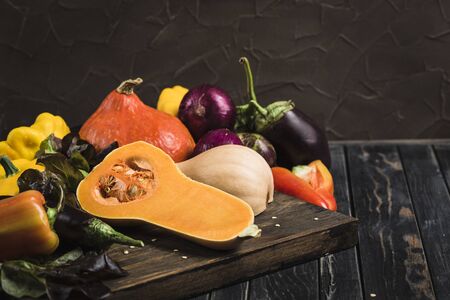 Fresh harvest of vegetables from pumpkin, eggplant, pepper, lettuce, red onion and squash on a dark wooden background close-up with a copy spaceの写真素材