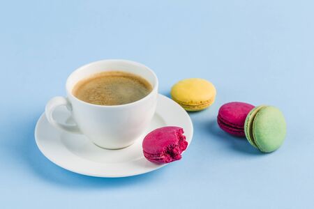 Colorful macaroons with a white Cup of coffee on a blue background, close-up, Flatley with copy space. Dessert with melon, lemon and raspberry flavor. Artの写真素材