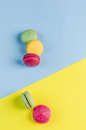 Multicolored macaroons on a blue and yellow background, top view, Flatley with copy space. Dessert with melon, lemon and raspberry flavor. Artの写真素材