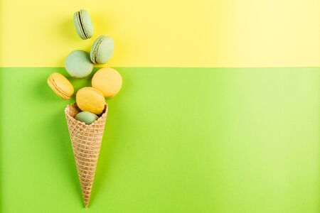 Multicolored macaroons in a waffle cone on a green and yellow background, top view, Flatley with copy space. Dessert with melon, lemon and raspberry flavor. Artの写真素材