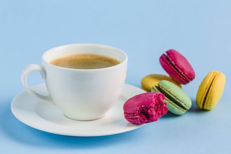Colorful macaroons with a white Cup of coffee on a blue background, close-up, Flatley with copy space. Dessert with melon, lemon and raspberry flavor. Artの写真素材