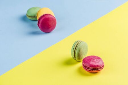 Multicolored macaroons on a blue and yellow background, top view, Flatley with copy space. Dessert with melon, lemon and raspberry flavor. Artの写真素材