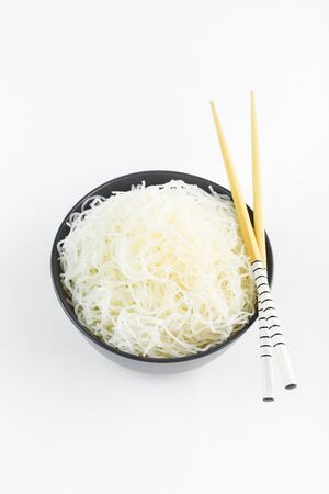 Cellophane rice noodles in a black bowl with chopsticks on white background, isolate, top view. Asian food. Copy space.の写真素材