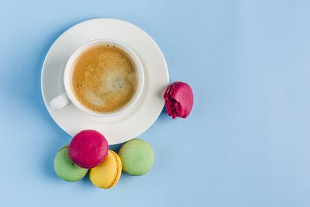 Multicolored macaroons with a white Cup of coffee on a blue background, top view, flat lay with copy space. Dessert with melon, lemon and raspberry flavor. Artの写真素材