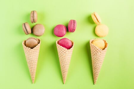 Multicolored macaroons in a waffle cone on a green and yellow background, top view, Flatley with copy space. Dessert with melon, lemon and raspberry flavor. Artの写真素材