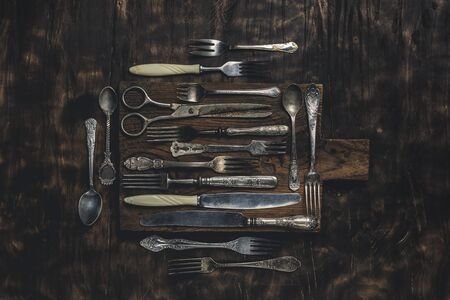 Vintage tableware on a wooden Board on a dark background. Forks, knives, spoons and scissors are items for serving the dining table. Copyspace. Horizontal orientation.の写真素材