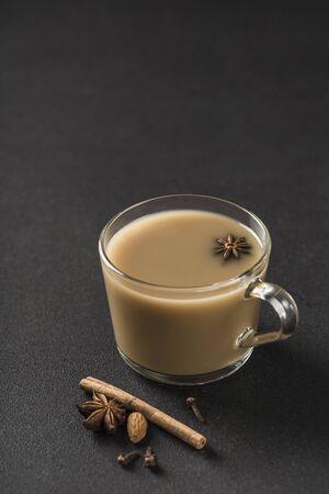 Popular Asian warming drink masala tea in a clear glass cup with coriander, cinnamon and rose stem on a black background. Closeup. Copyspace. Vertical orientation.の写真素材