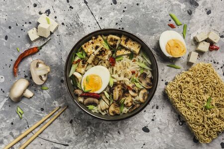 Noodle bowl with mushrooms, egg, tofu cheese, chopsticks and ingredients on a gray background. Asian food. Top view with copyspace. Horizontal orientation.の写真素材