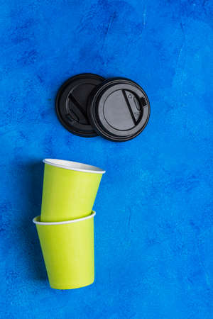 Two green paper reusable coffee cups with black lids on a classic blue background. Zero waste concept top view with copy space. Vertical orientation.の写真素材