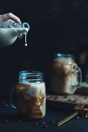 Iced coffee with milk in glasses with a handle, a great refreshing drink on a dark background. Close-up with copy space. Vertical orientation.の写真素材