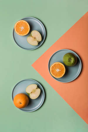 Orange and Apple on flat plates on a colored green-orange background. Concept of healthy nutrition and vitamins. Flat lay with copy space. Vertical orientation.の写真素材