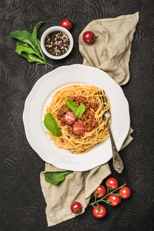 Delicious classic Italian Bolognese pasta with tomatoes and Basil on a plate on a dark background. Top view, vertical orientation.の写真素材