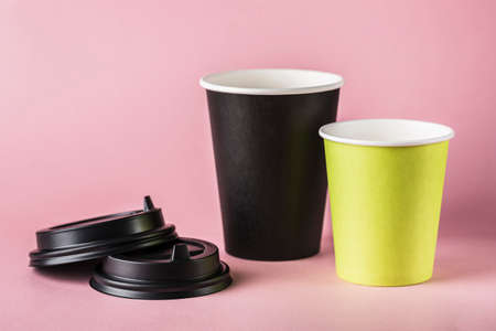 Some green and black paper reusable coffee cups with lids on a pink background. Zero waste concept...