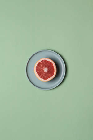 Grapefruit on a flat plate on a colored light green background. Concept of healthy nutrition and vitamins. Flat lay with copy space. Vertical orientation.の写真素材