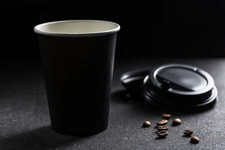 A silhouette of a paper refillable coffee Cup with an open lid and coffee beans on a black background. Zero waste concept close-up with copy space. Horizontal orientation.の写真素材
