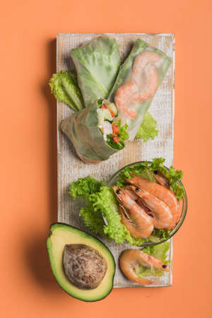 Spring rice paper roll with shrimp, avocado, paprika, lettuce and cottage cheese on a wooden white...