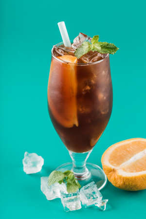 Refreshing iced coffee with orange and mint in a glass with a tube on a bright background. Coffee drink to quench your thirst on a hot day. Close up. Vertical orientation.の写真素材