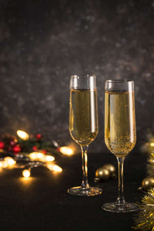 New year 2021 - two glasses of champagne on a dark background with bokeh from garlands. Classic alcoholic drink for a new year's holiday atmosphere. Vertical orientation with a copyspace.の写真素材