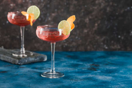 Alcoholic Margarita cocktail with ice frappe, lime slice and orange zest on a dark background. Horizontal orientation with a copy space.の写真素材