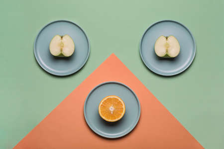 Orange and Apple on flat plates on a colored green-orange background. Concept of healthy nutrition and vitamins. Flat lay with copy space. Horizontal orientation.の写真素材