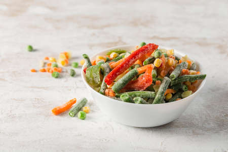 Frozen vegetables: a mix of vegetables, string beans and cauliflower in a white bowl on a light background. Close-up with a copy space. Horizontal orientation.の写真素材