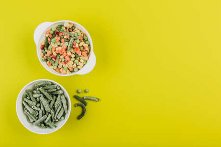 Frozen vegetables: string beans and a mix of vegetables in white bowls on a bright yellow background. Top view with a copy space. Horizontal orientation.の写真素材