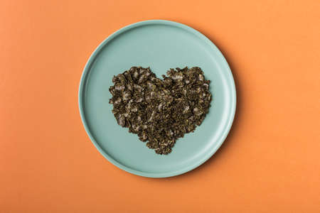 Hemp flakes in a flat dish in the form of a heart on an orange background. flatlay with copy space. Cannabis food concept. Horizontal orientation.の写真素材